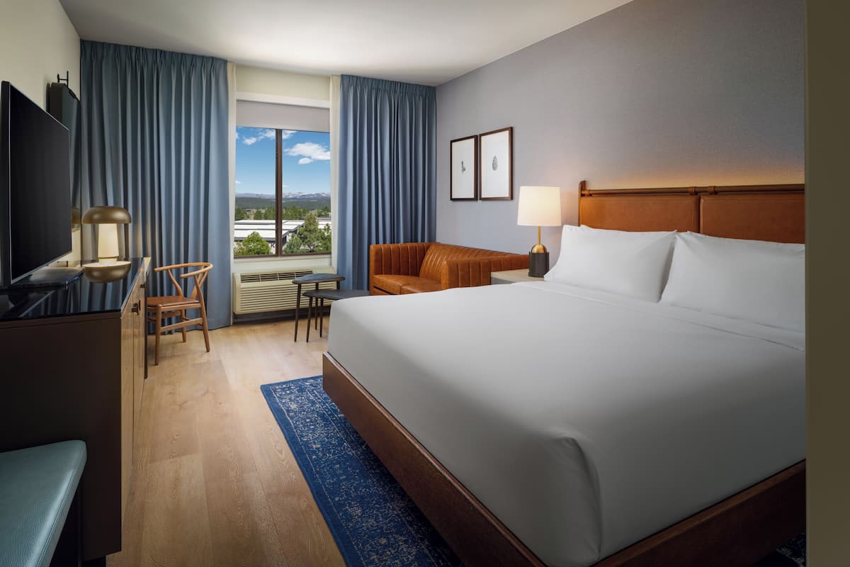 A hotel room with a large bed, a desk with a chair, a television, and a window with curtains.