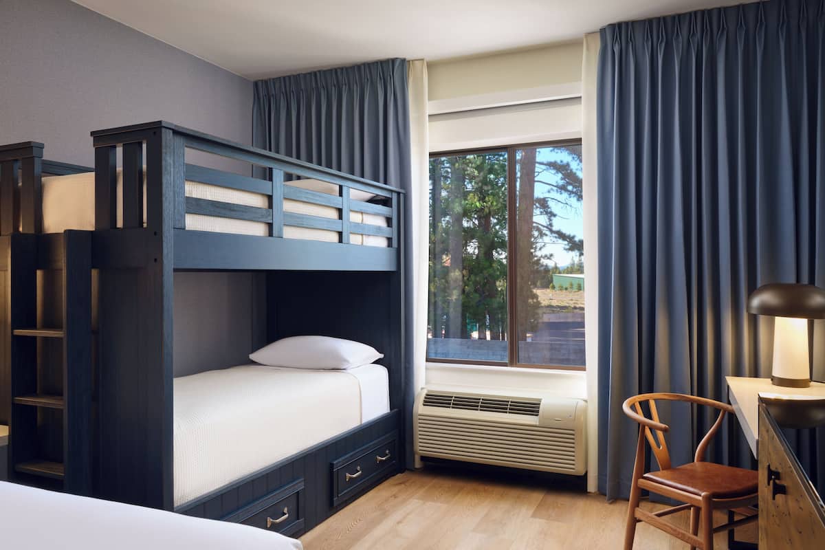 A bedroom with a bunk bed, a desk, a chair, and a window with curtains.