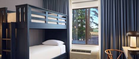 A bedroom with a bunk bed, a desk, a chair, and a window with curtains.