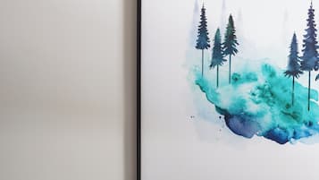 A framed artwork of trees and a landscape on a white wall, a brown leather sofa with two pillows, and a white wall.