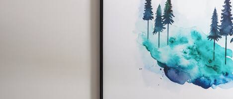 A framed artwork of trees and a landscape on a white wall, a brown leather sofa with two pillows, and a white wall.