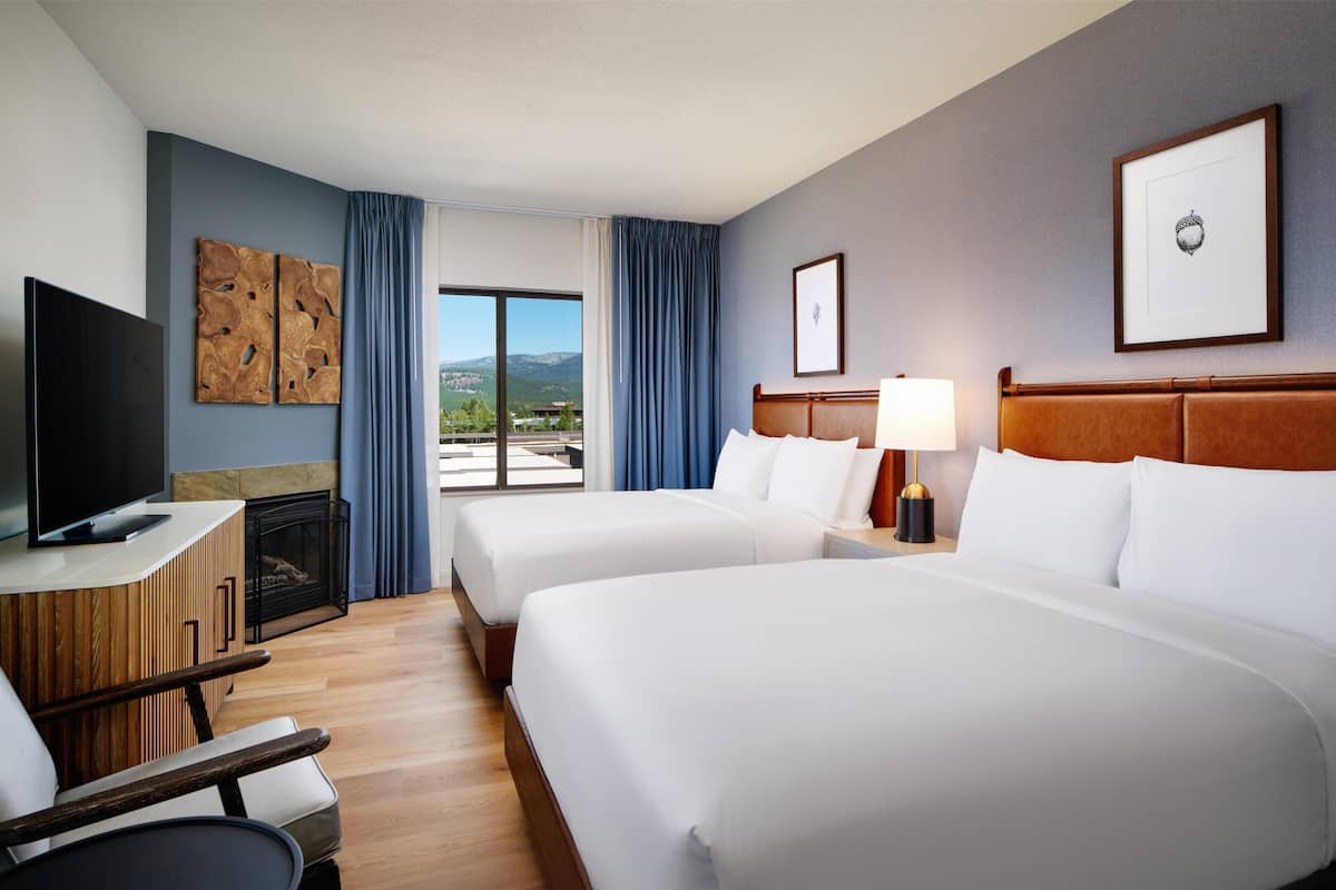 A hotel room with two beds, a TV, a fireplace, and a view of the outdoors.