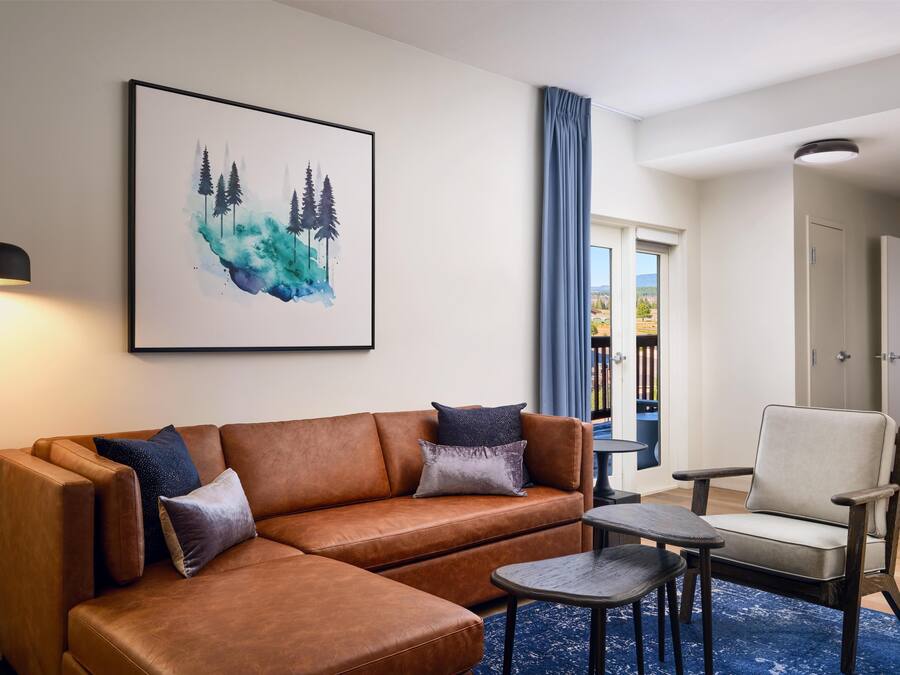 Una sala de estar con un sofá de cuero marrón, una silla, una mesa pequeña y un cuadro de árboles en la pared.