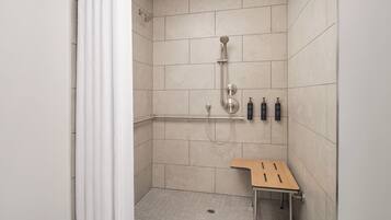 A shower area with a handheld showerhead, a wall-mounted faucet, and a small wooden bench.