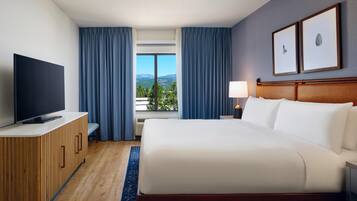 A hotel room with a bed, a TV, a desk, a lamp, and a window with curtains.