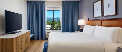 Une chambre d’hôtel équipée d’un lit, d’une télévision, d’un bureau, d’une lampe et d’une fenêtre avec des rideaux.