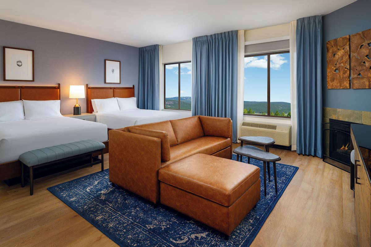 A hotel room with two beds, a sofa, a bench, a fireplace, and a view of the mountains.