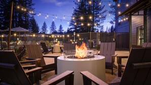 An outdoor seating area with chairs and a central fire feature, surrounded by string lights and trees.