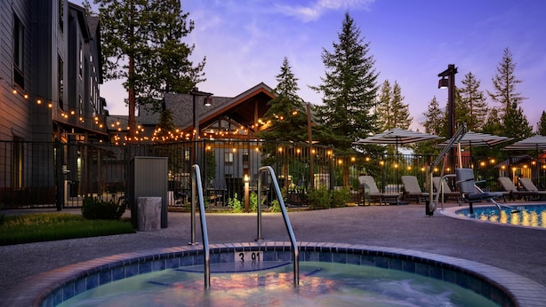 A hot tub surrounded by lounge chairs and umbrellas, with a pool in the background.