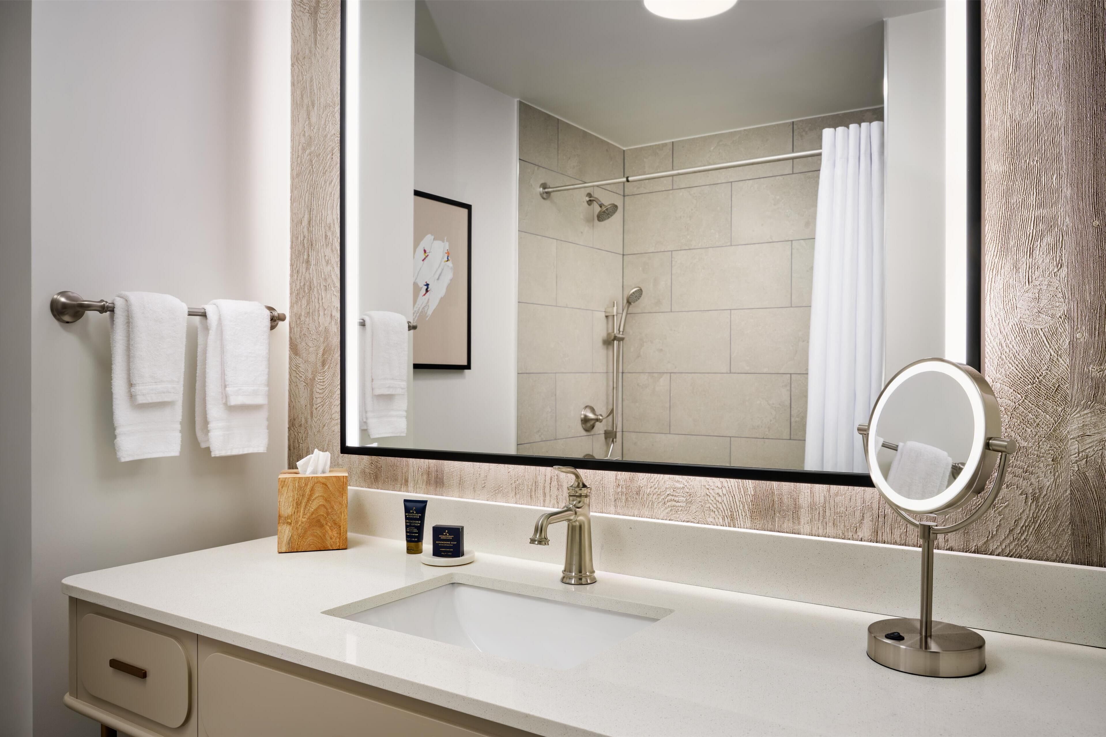A bathroom with a large mirror, a sink, a towel rack, and a shower area.