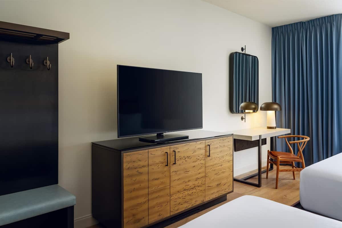 A hotel room with a flat-screen TV, wooden cabinet, desk, chair, and a bed.