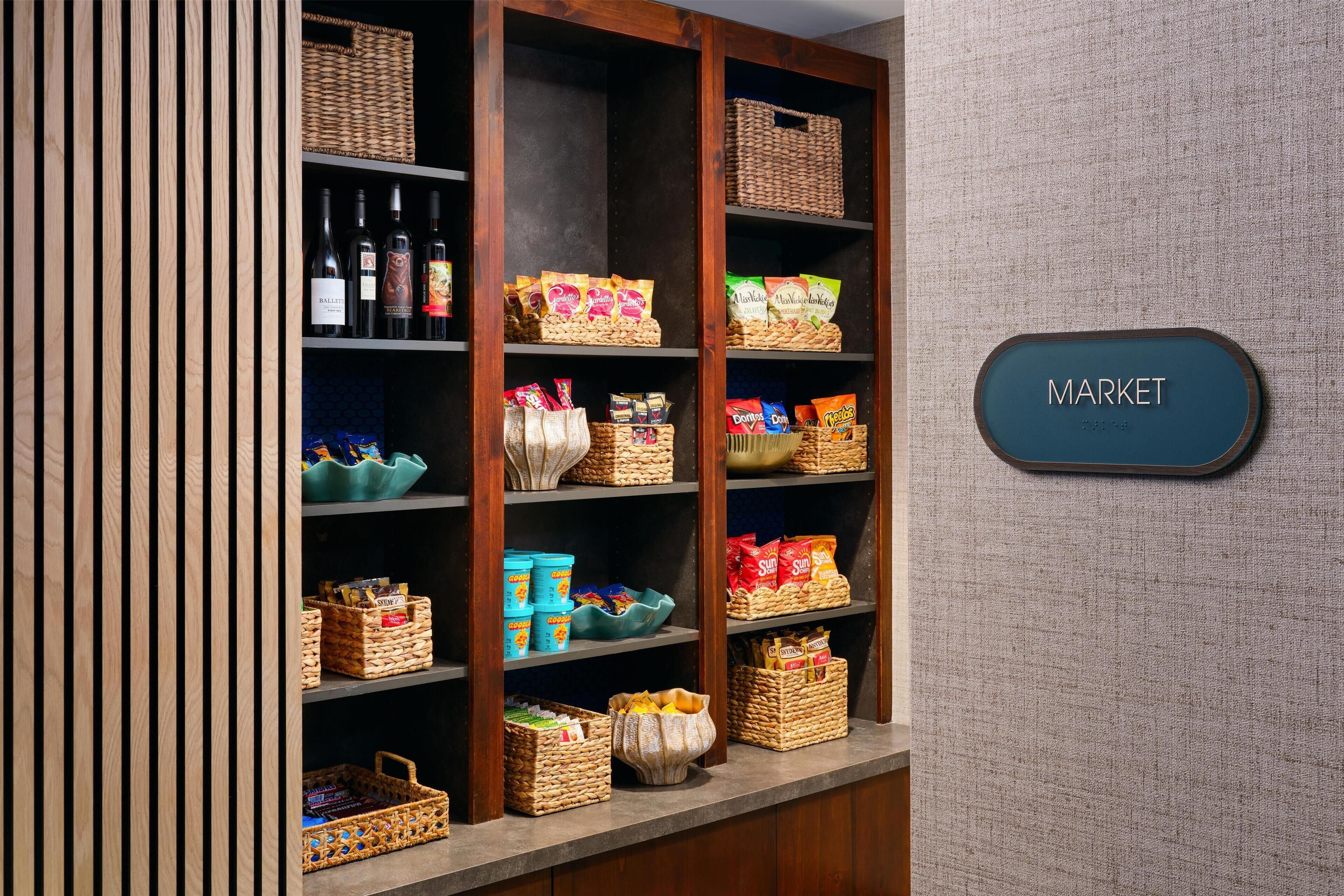 A wooden shelf unit with baskets and snacks, a sign labeled 'MARKET,' and a textured wall.