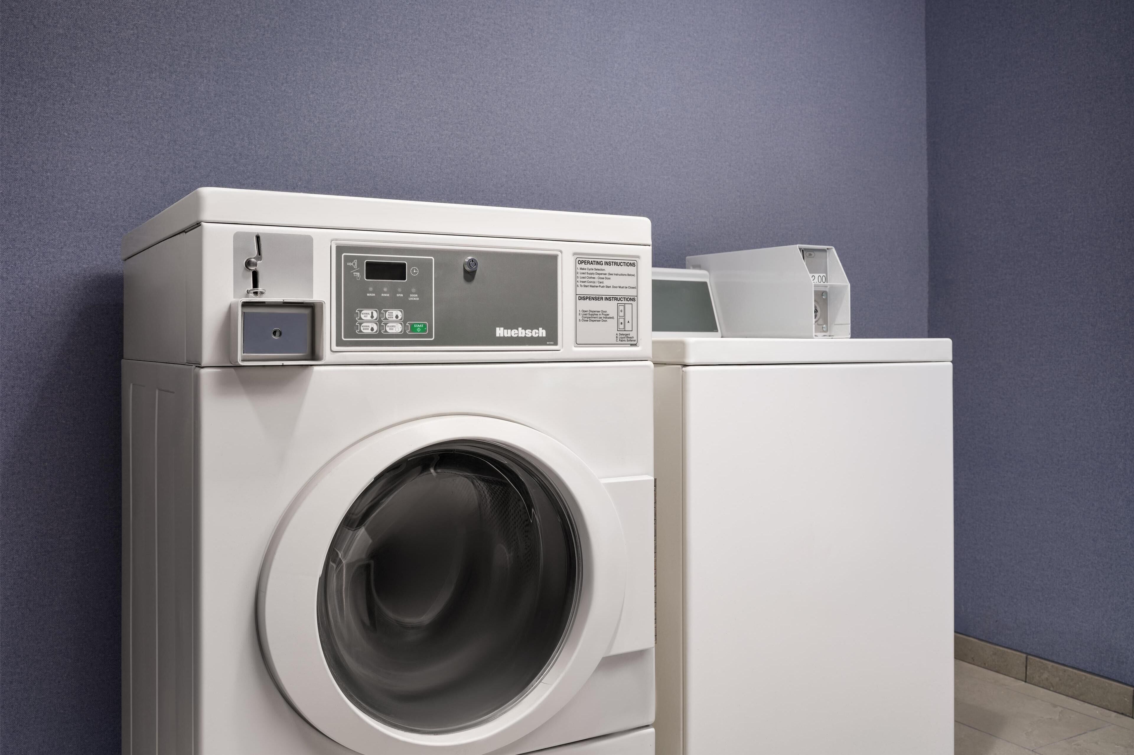 Une machine à laver blanche à chargement frontal, dotée d’un panneau de commande, est placée contre un mur bleu.