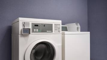 Une machine à laver blanche à chargement frontal, dotée d’un panneau de commande, est placée contre un mur bleu.