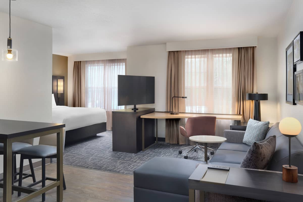 Una habitación de hotel con cama, escritorio, silla, sofá, reposapiés y televisor.