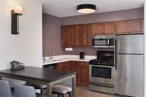 Una cocina moderna con armarios de madera, electrodomésticos de acero inoxidable, una mesa de comedor con sillas y una lámpara fijada a la pared.