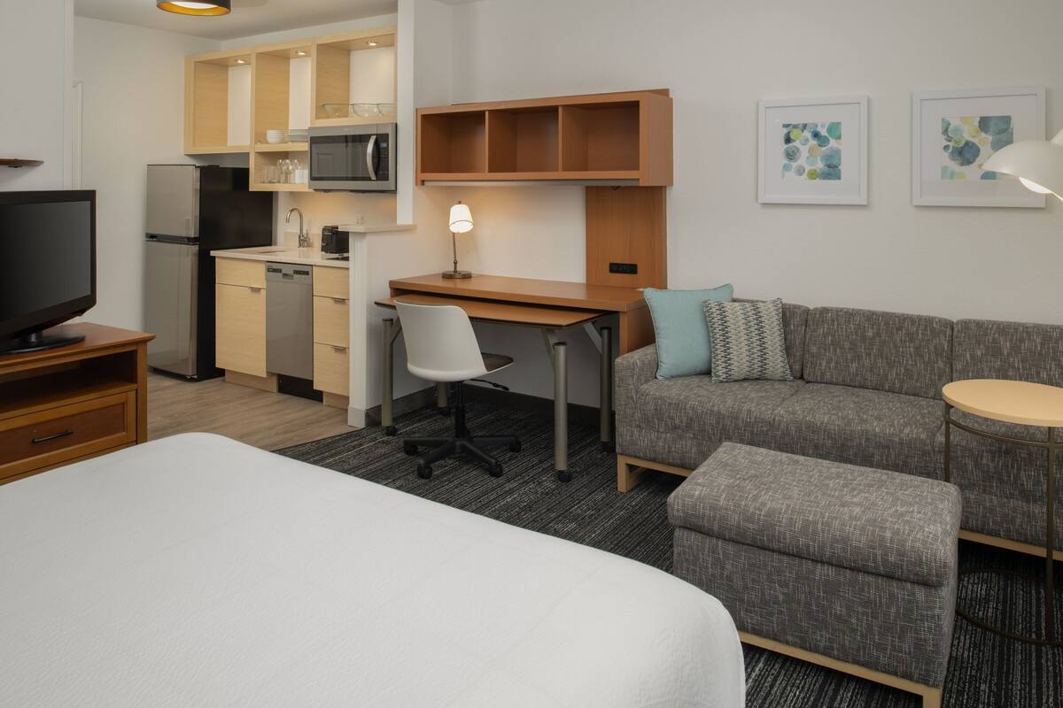 Habitación de hotel con cama, escritorio y silla, kitchenette, sofá y una mesita.