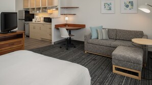 Une chambre d’hôtel comprenant un lit, un bureau avec une chaise, un canapé, une petite table et une kitchenette.