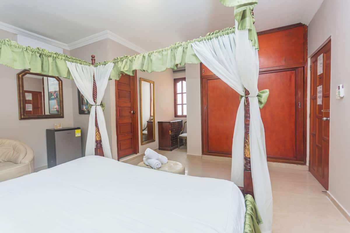 A hotel room with a large bed, a desk, a chair, a wardrobe, and a mirror.