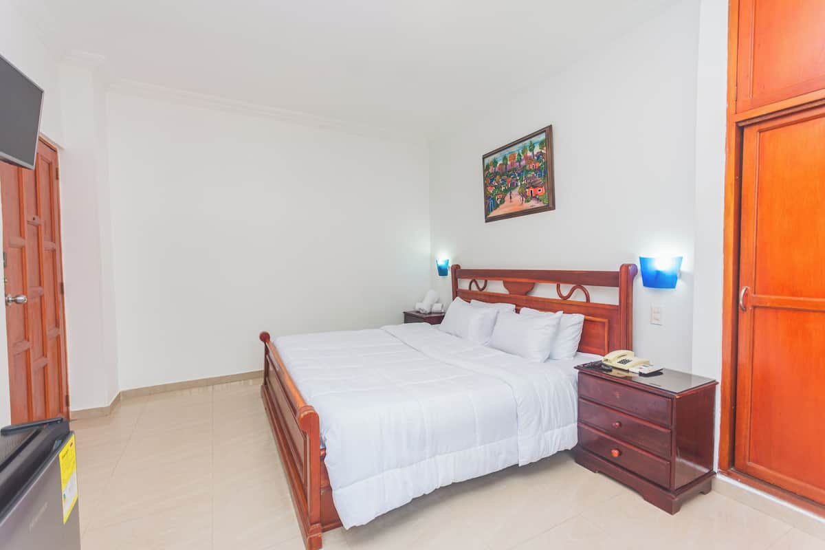 A bedroom with a wooden bed, a nightstand, a wall-mounted lamp, and a door.