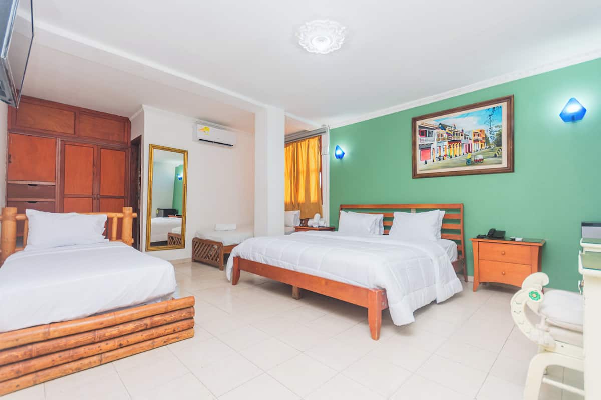 A hotel room with two beds, a wooden headboard, a green accent wall, a painting, a nightstand, and a small table.