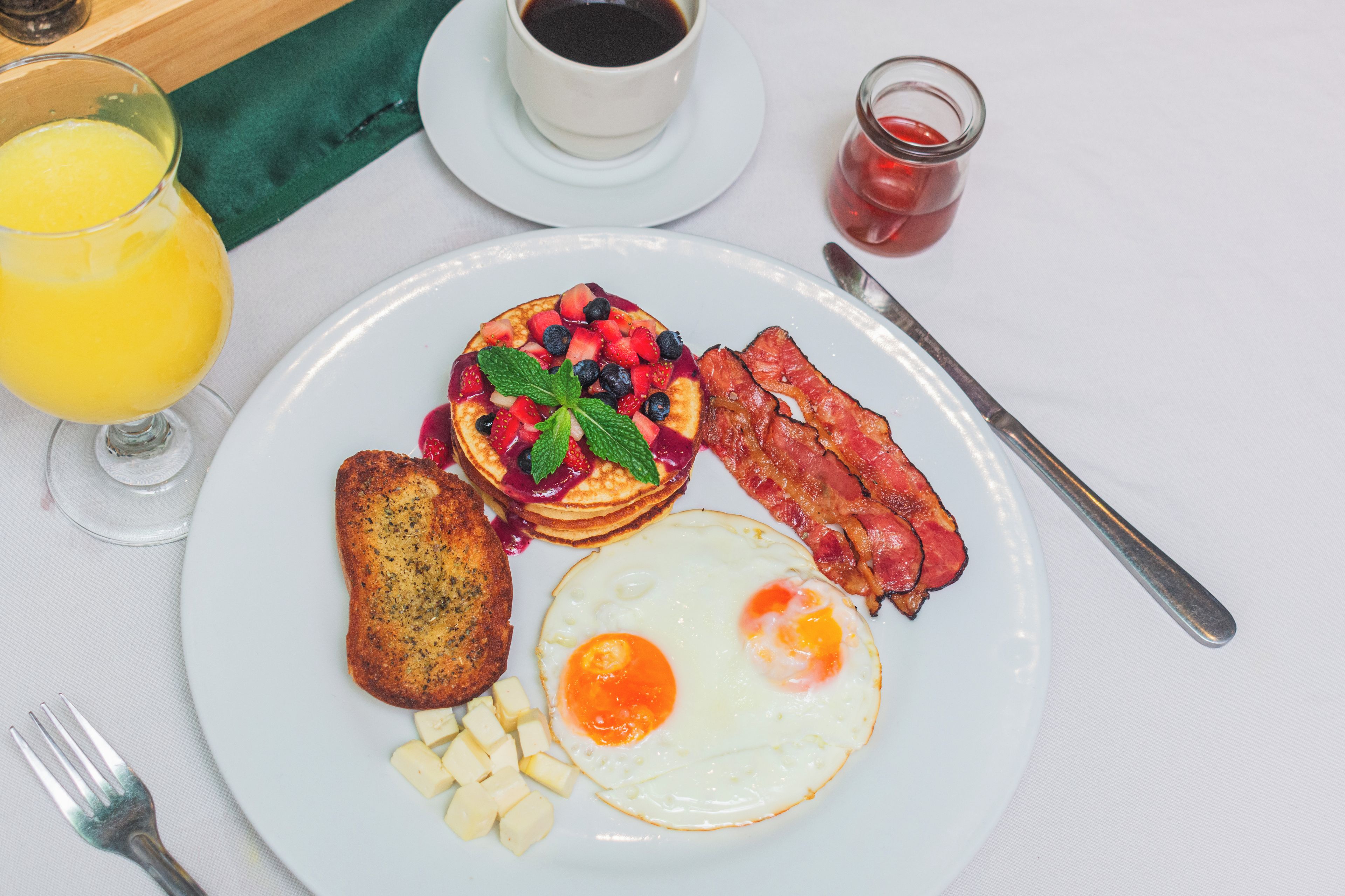 A breakfast plate with pancakes, eggs, bacon, toast, and fruit.