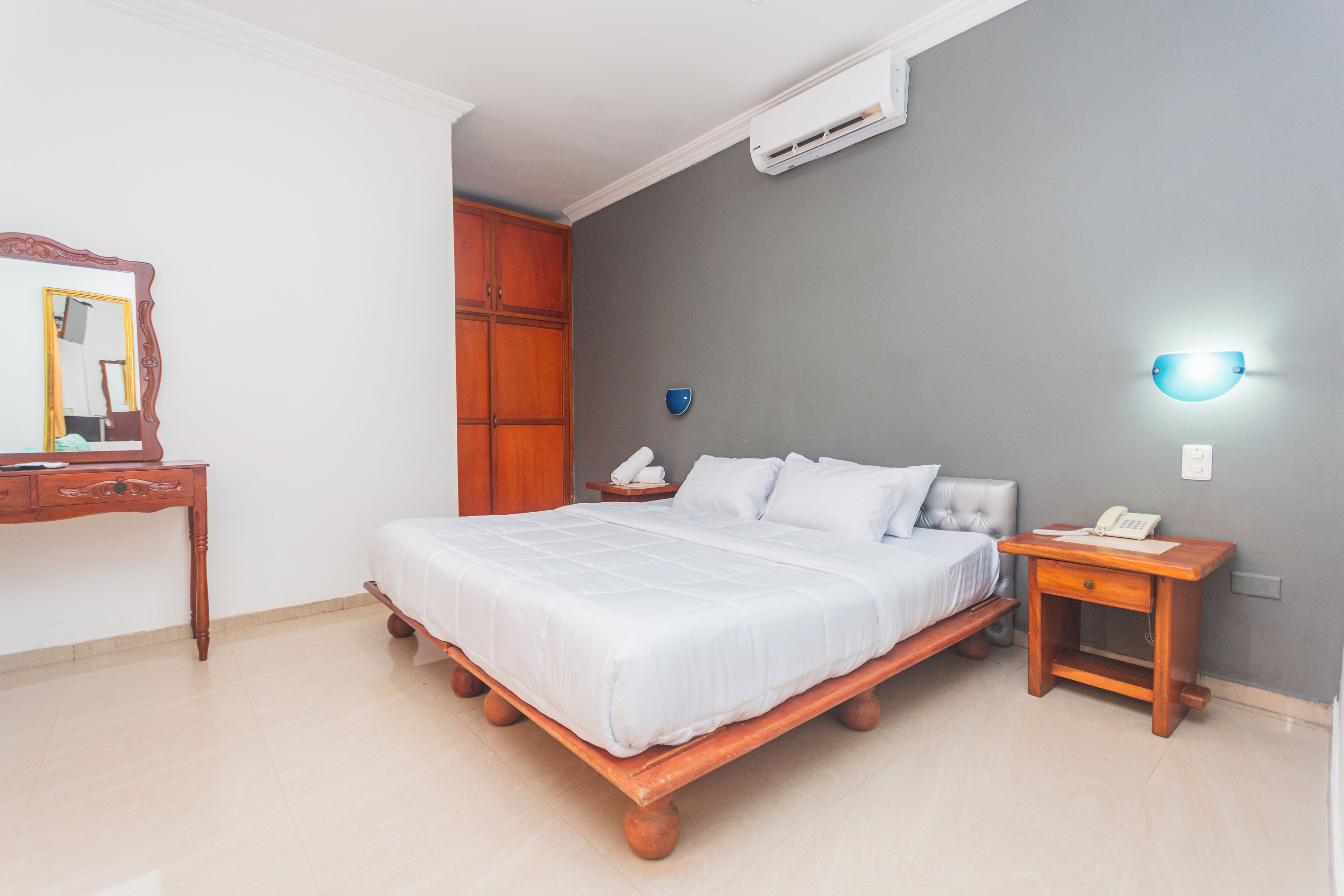 A bedroom with a bed, a wooden nightstand, a bedside table, a mirror, and a wardrobe.