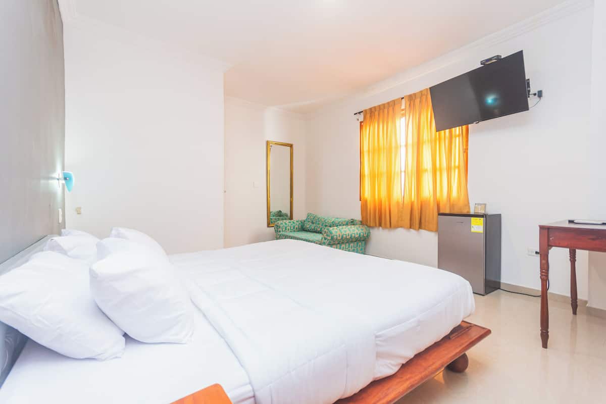 A hotel room with a bed, a desk, a television mounted on the wall, and a small refrigerator.