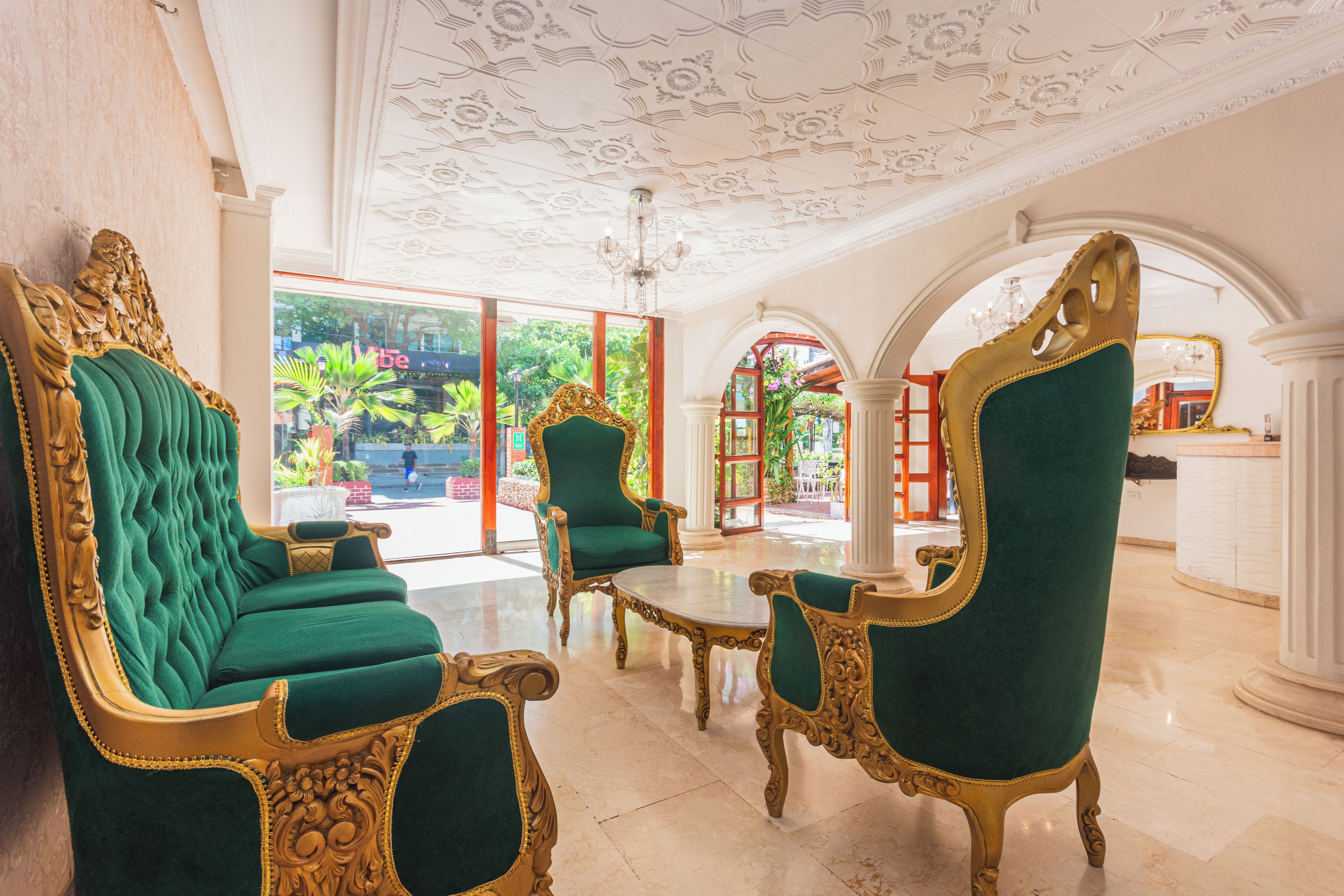 A luxurious lobby with ornate green upholstered chairs, a marble floor, and a decorative ceiling.
