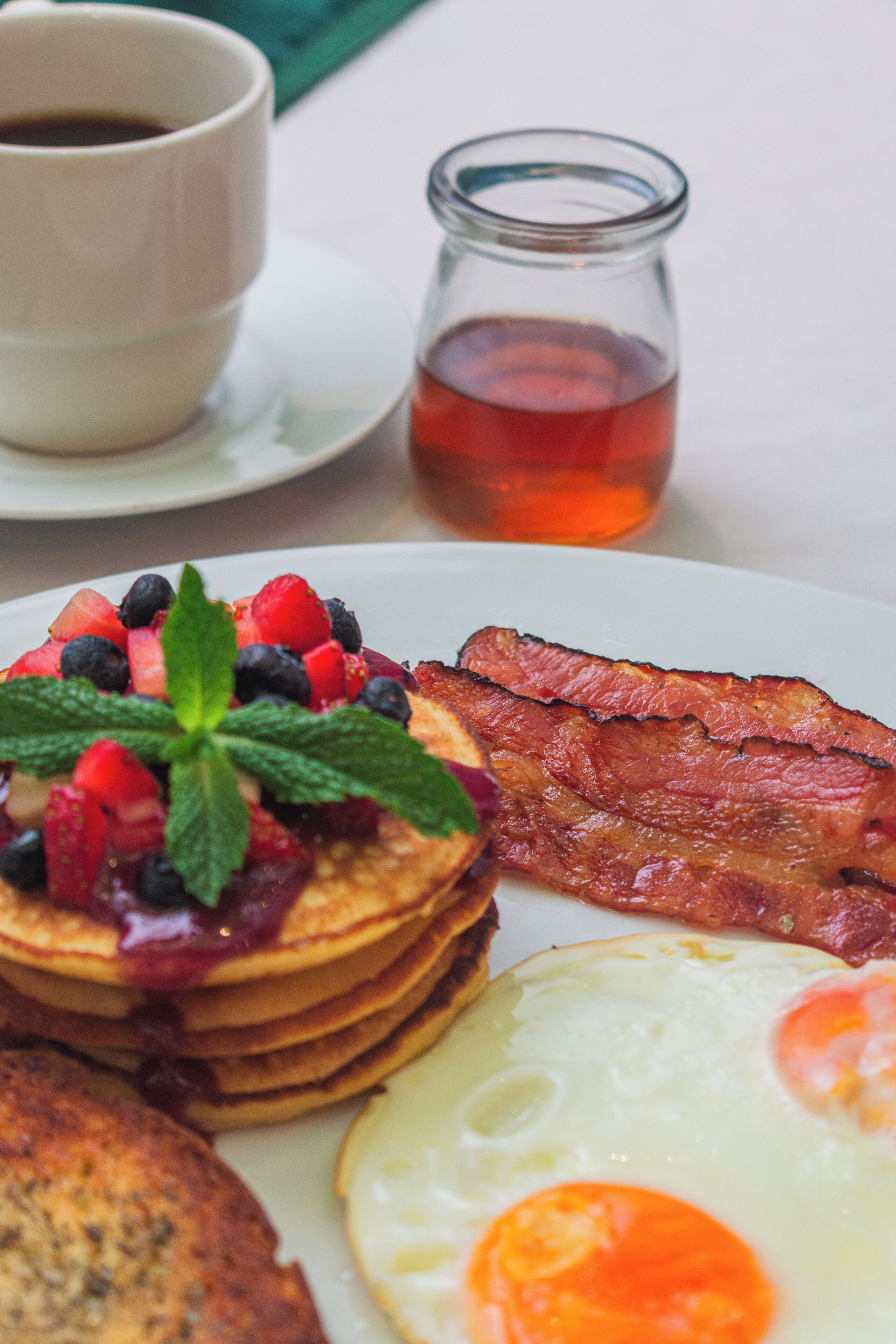 Un piatto colazione con pancake, pancetta, un uovo fritto e frutti di bosco freschi.