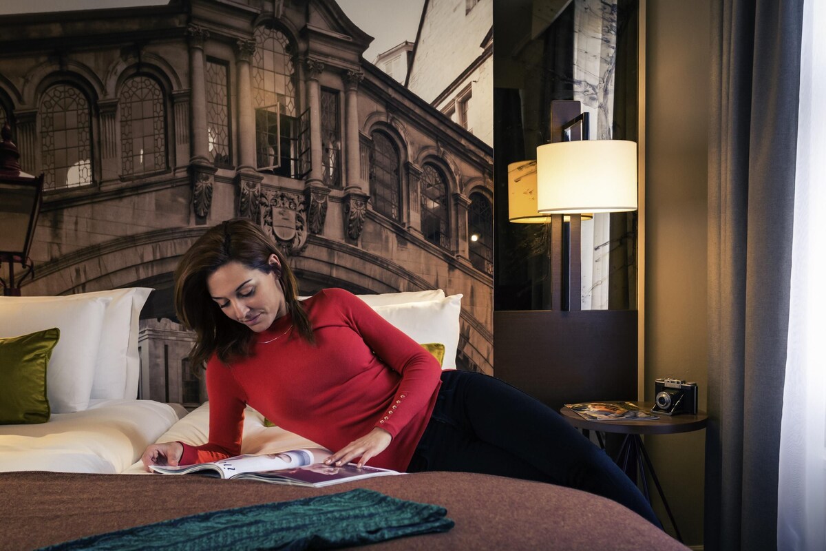 A hotel room with a bed, a reading lamp, and a wall mural.