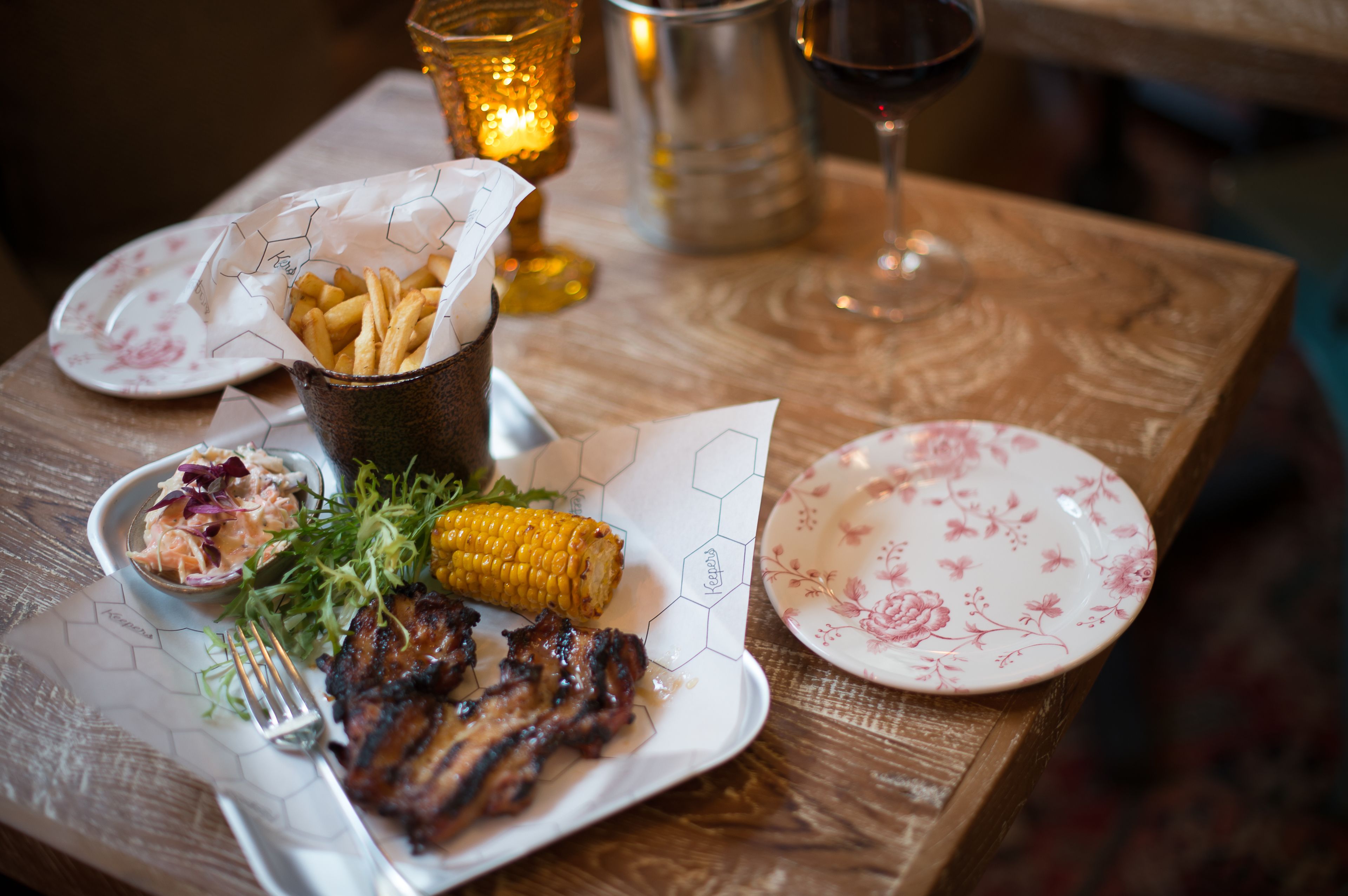 Ein Holztisch mit gegrilltem Fleisch, Maiskolben und einer kleinen Salat-Schale.