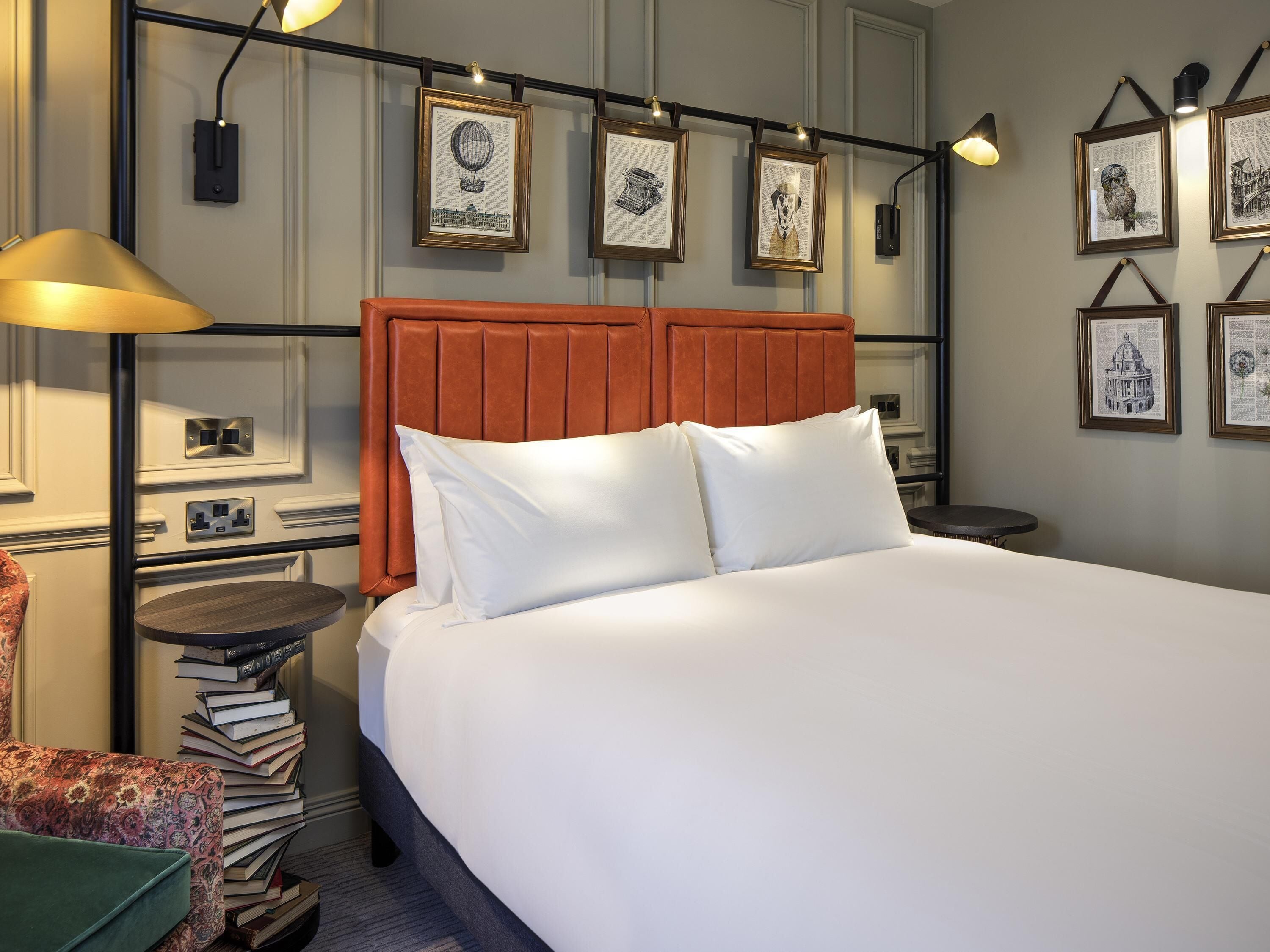 Een netjes ingerichte hotelkamer met een bed, nachtkastjes, een lamp en ingelijste foto’s aan de muur.