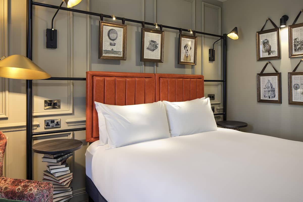 Een netjes ingerichte hotelkamer met een bed, nachtkastjes, een lamp en ingelijste foto’s aan de muur.