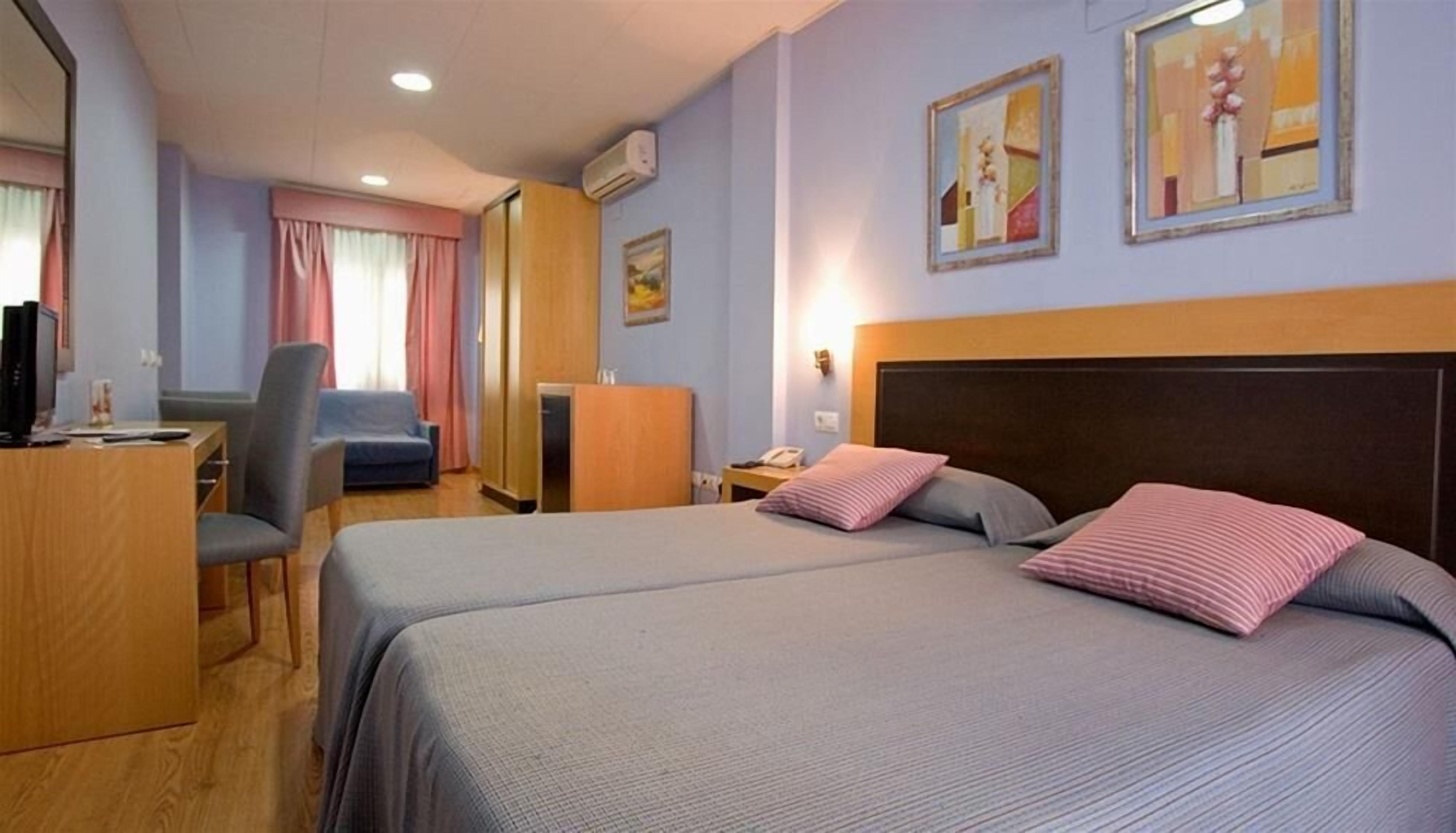 A hotel room with two beds, a desk, a chair, and a TV.