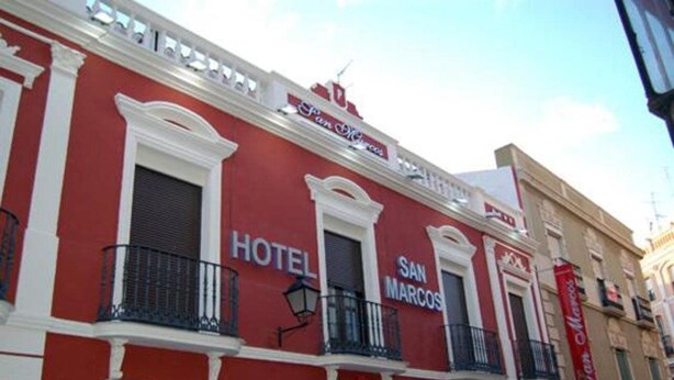 A red building with "HOTEL SAN MARCOS" signage, white trim, and black balconies. - San Marcos (Badajoz)