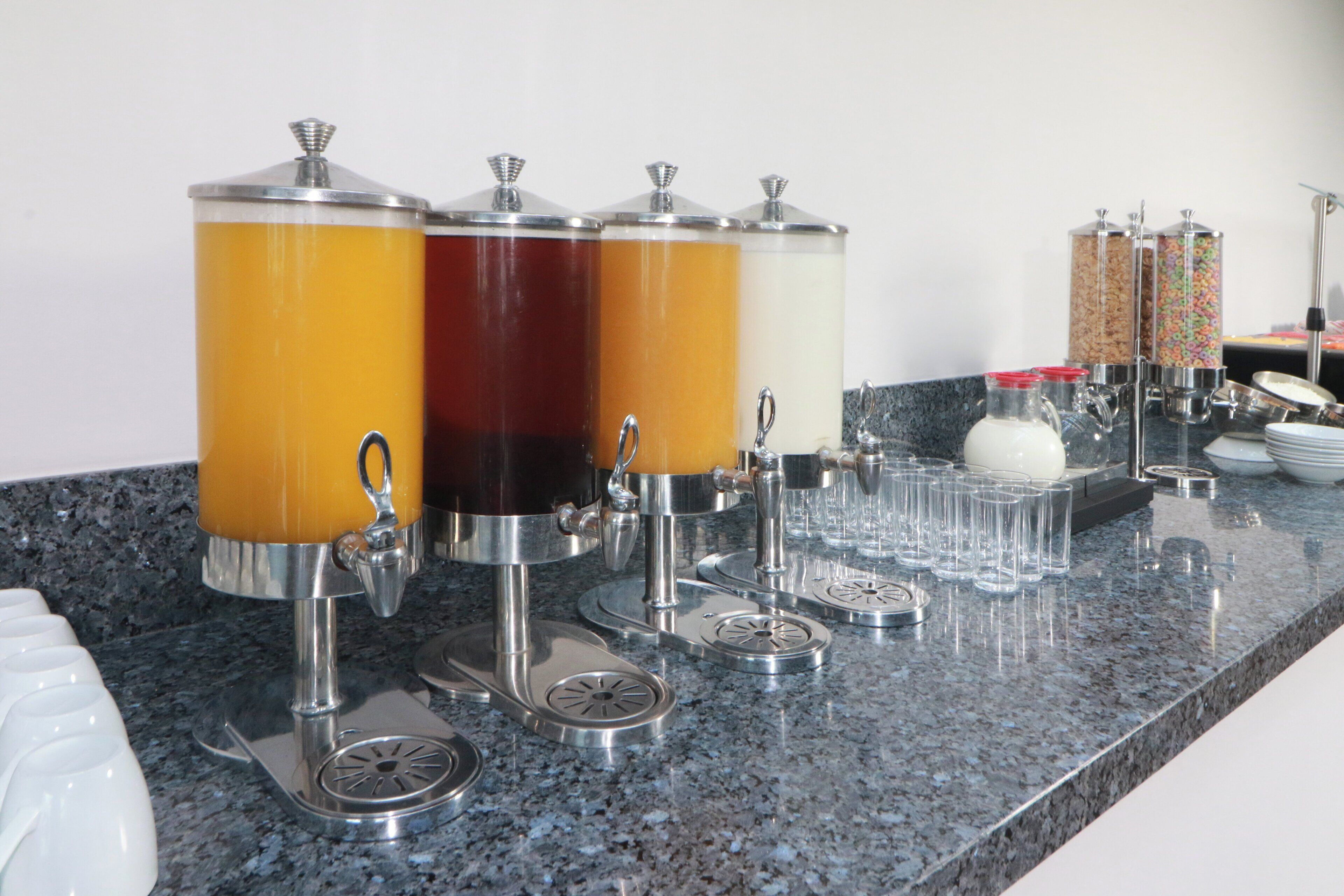 Una estación de bebidas con dispensadores y vasos sobre una encimera de granito.