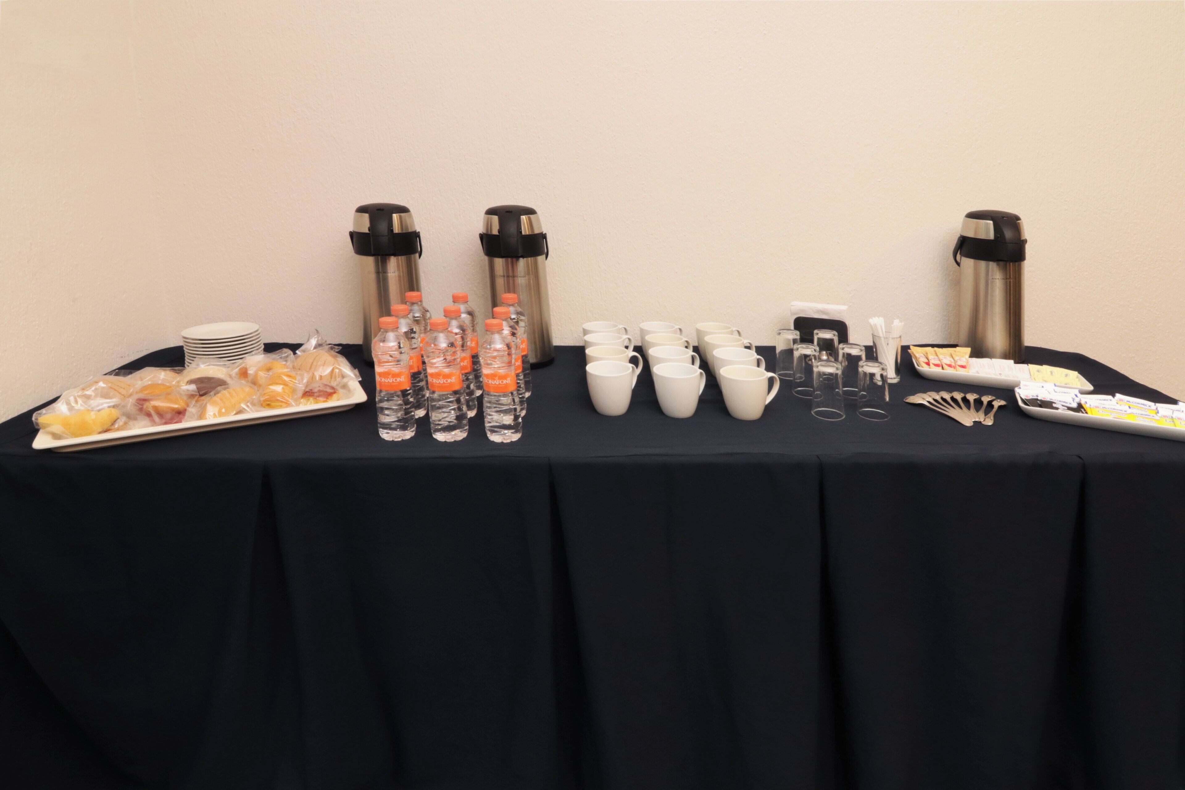 Una mesa de buffet con comida, botellas de agua, tazas de café y termos.