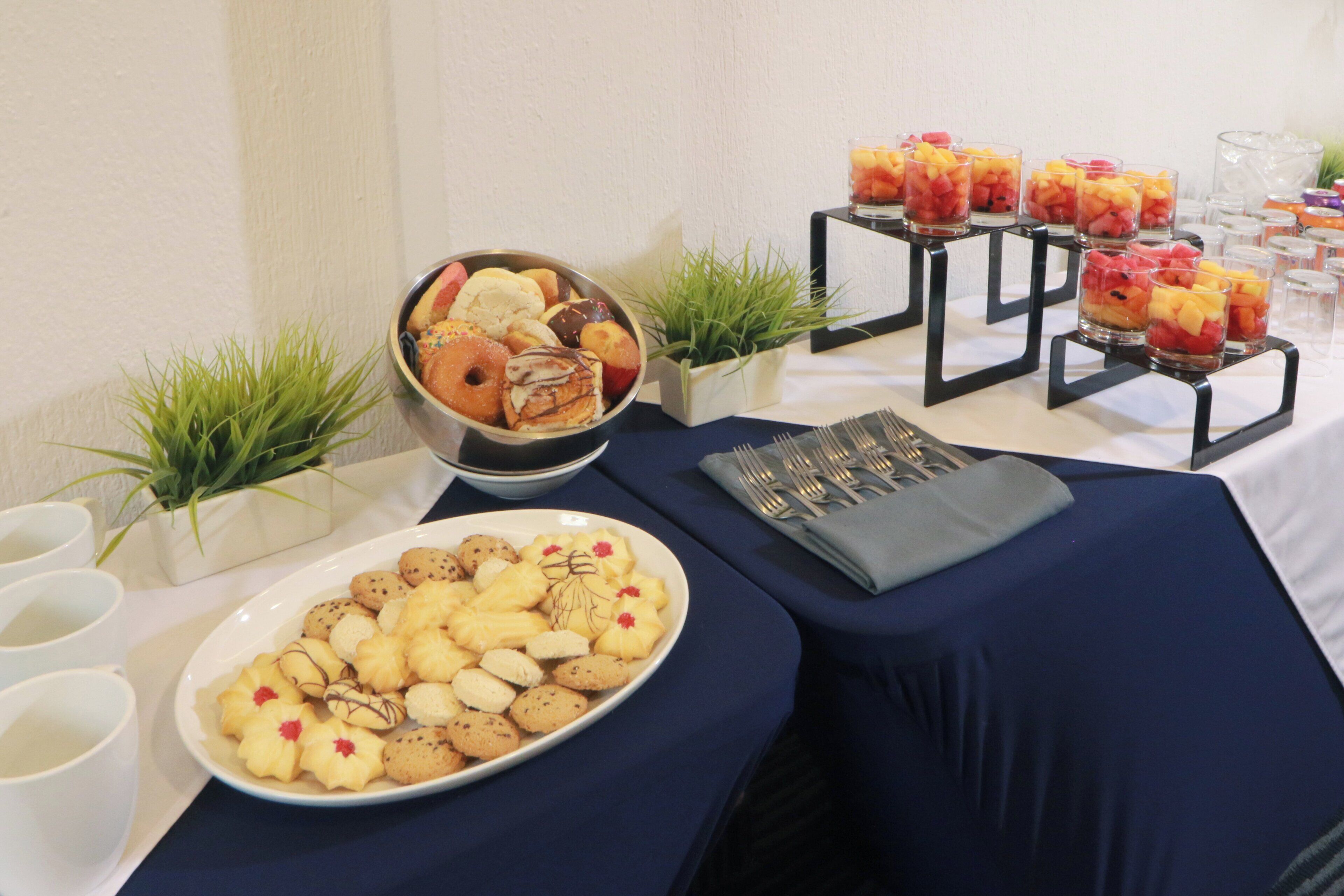 Une table de buffet proposant divers plats, notamment une assiette de biscuits, un saladier de pâtisseries et des coupes de fruits.