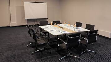 A conference room with a whiteboard, a projector screen, a table with chairs, water bottles, and documents.