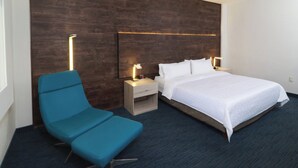 Ein Hotelzimmer mit einem Bett, einem Nachttisch mit Lampe, einem Sessel und einer Wandleuchte.