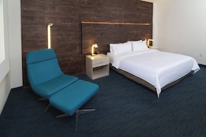 Une chambre d’hôtel comprenant un lit, une table de chevet avec une lampe, une chaise et un luminaire fixé au mur.