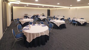 Ein Konferenzraum mit mehreren runden Tischen, die jeweils mit einer weißen Tischdecke bedeckt und von blauen Stühlen umgeben sind.