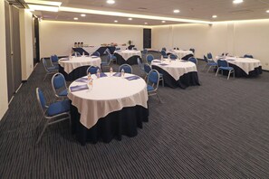Une salle de conférence dotée de plusieurs tables rondes, chacune recouverte d’une nappe blanche et entourée de chaises bleues.