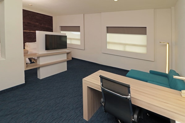 A modern hotel room with a desk, chair, television, and a sofa.