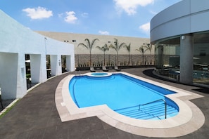 A swimming pool with a curved design, surrounded by a low wall and palm trees. - Holiday Inn Express San Luis Potosi by IHG (San Luis Potosi)