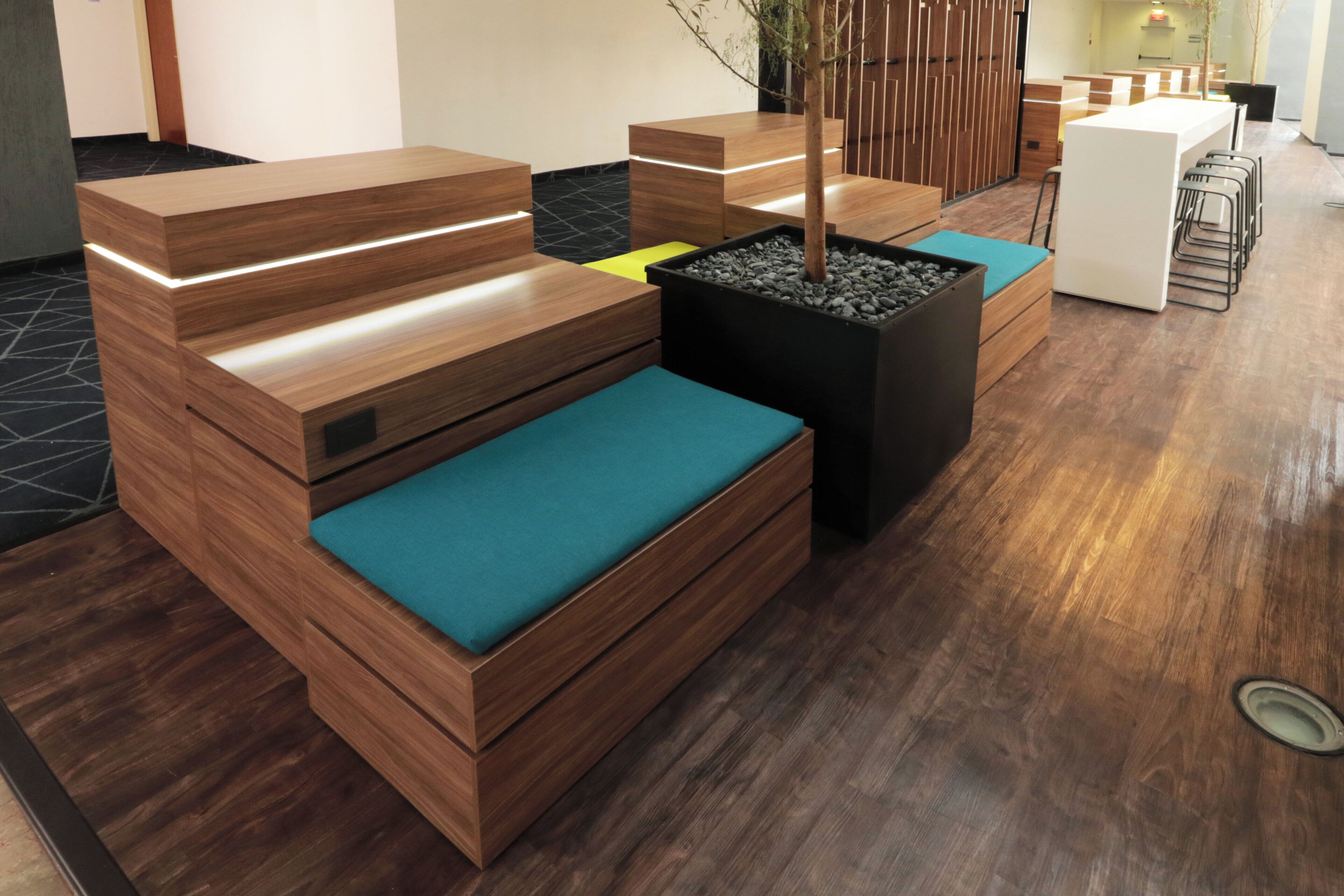 A modern reception area with wooden reception desks, a seating area with teal cushions, and a potted plant.