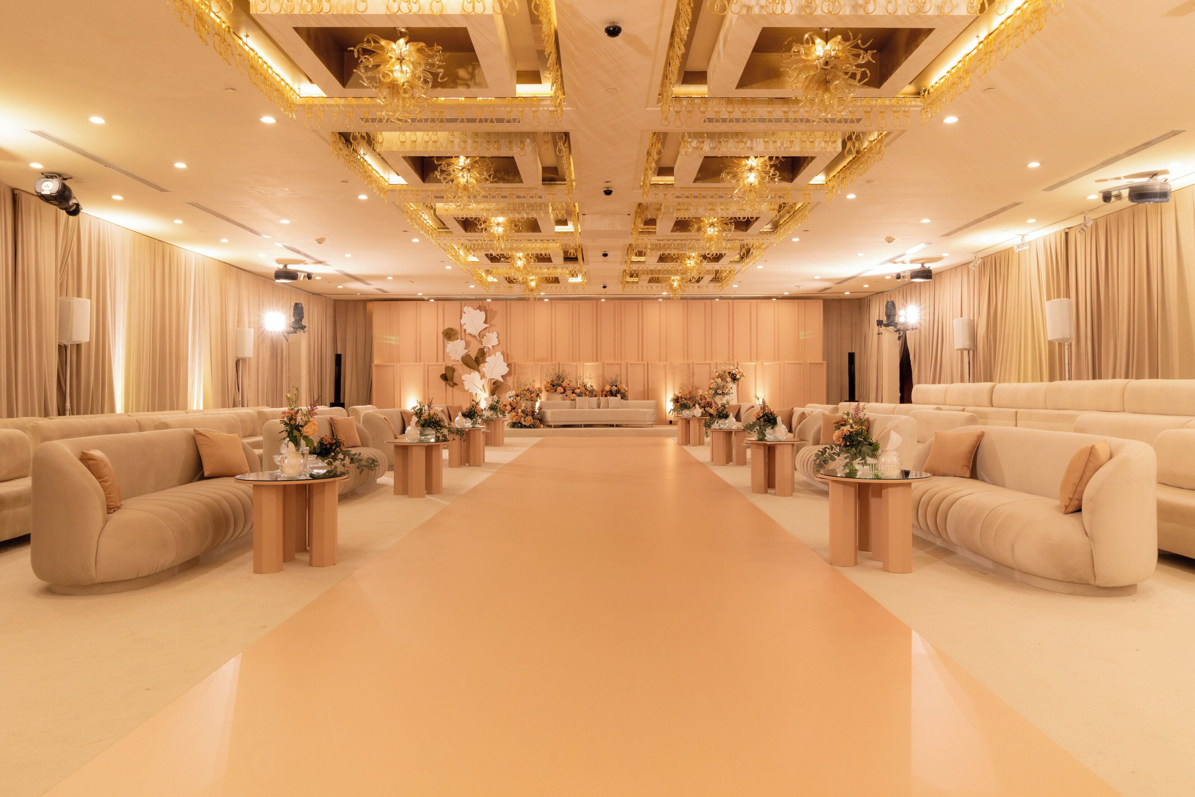 A spacious room with a central seating area, multiple tables with floral centerpieces, and a decorative ceiling with recessed lighting.