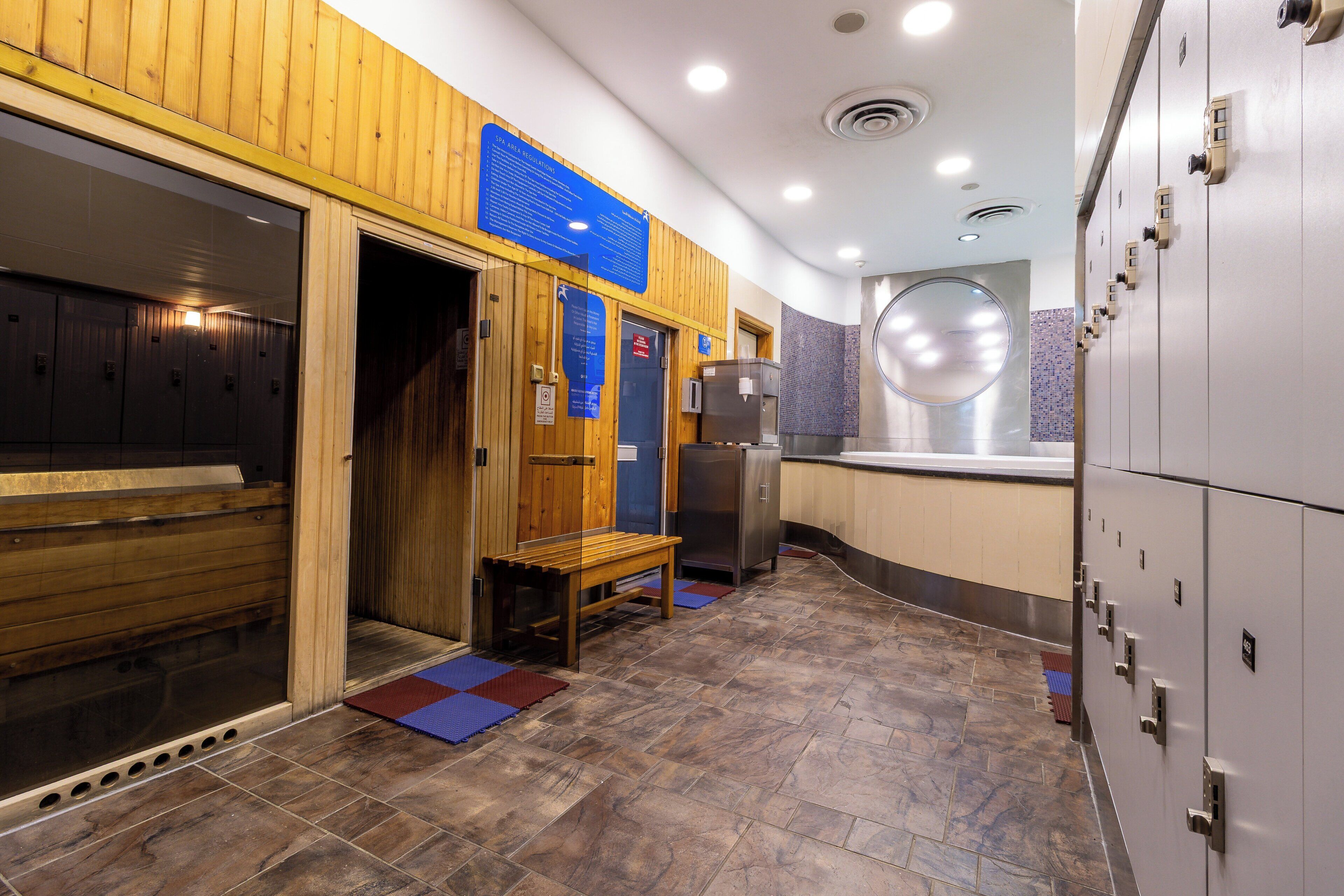 A sauna room with wooden benches, a bench, a refrigerator, and lockers.
