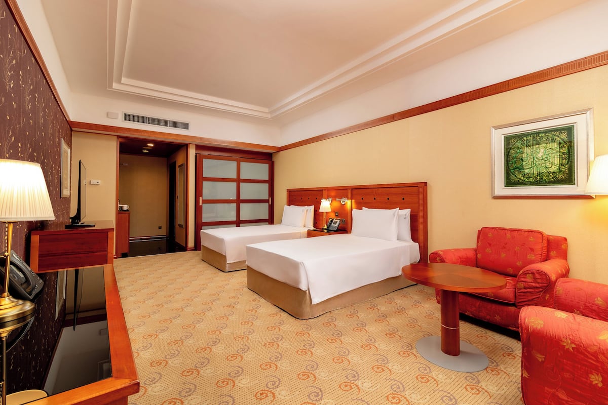 A hotel room with two beds, a red sofa, a small table, and a lamp.